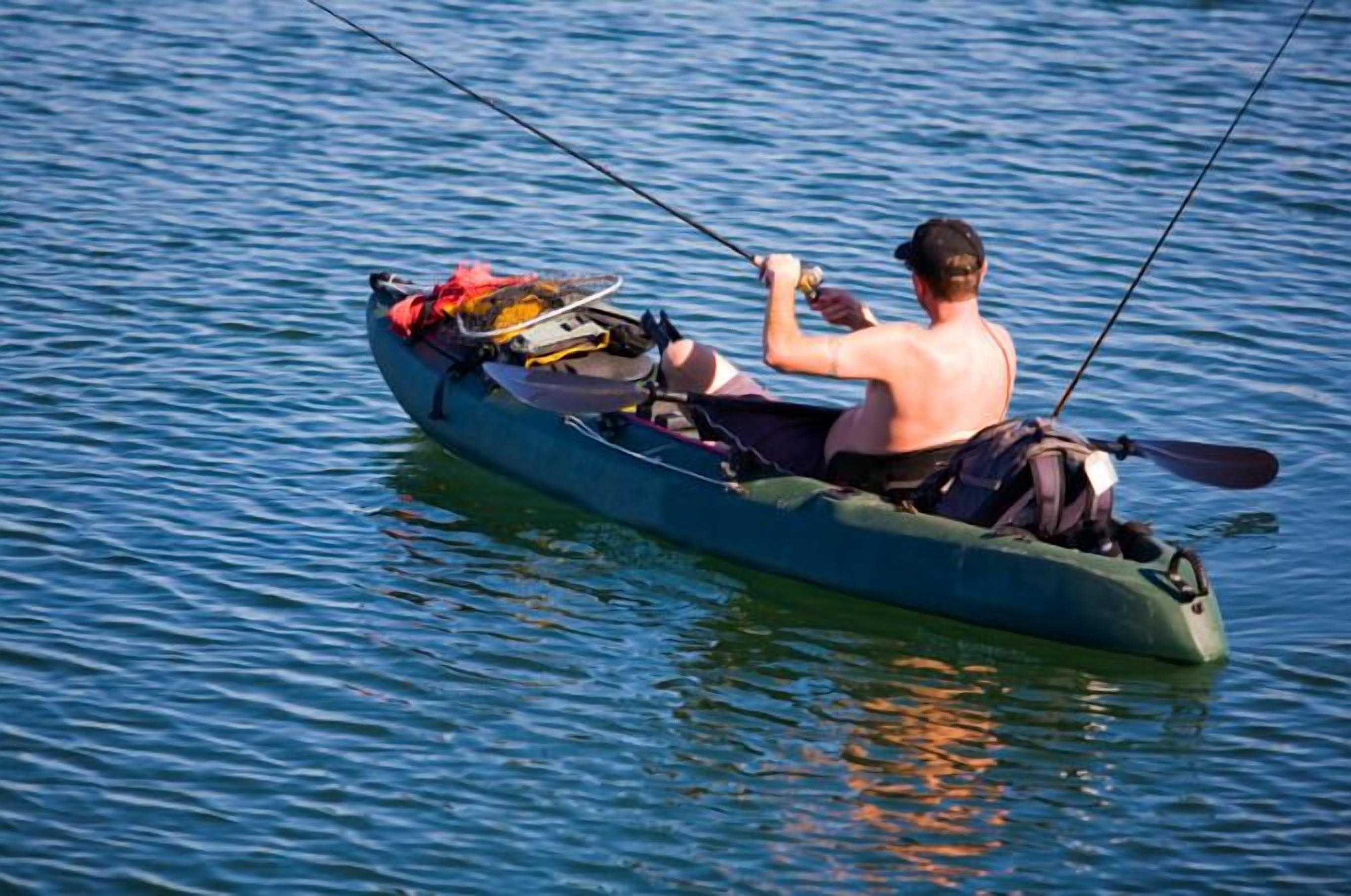 Une personne est assise dans un kayak sur une étendue d’eau calme et tient une canne à pêche.