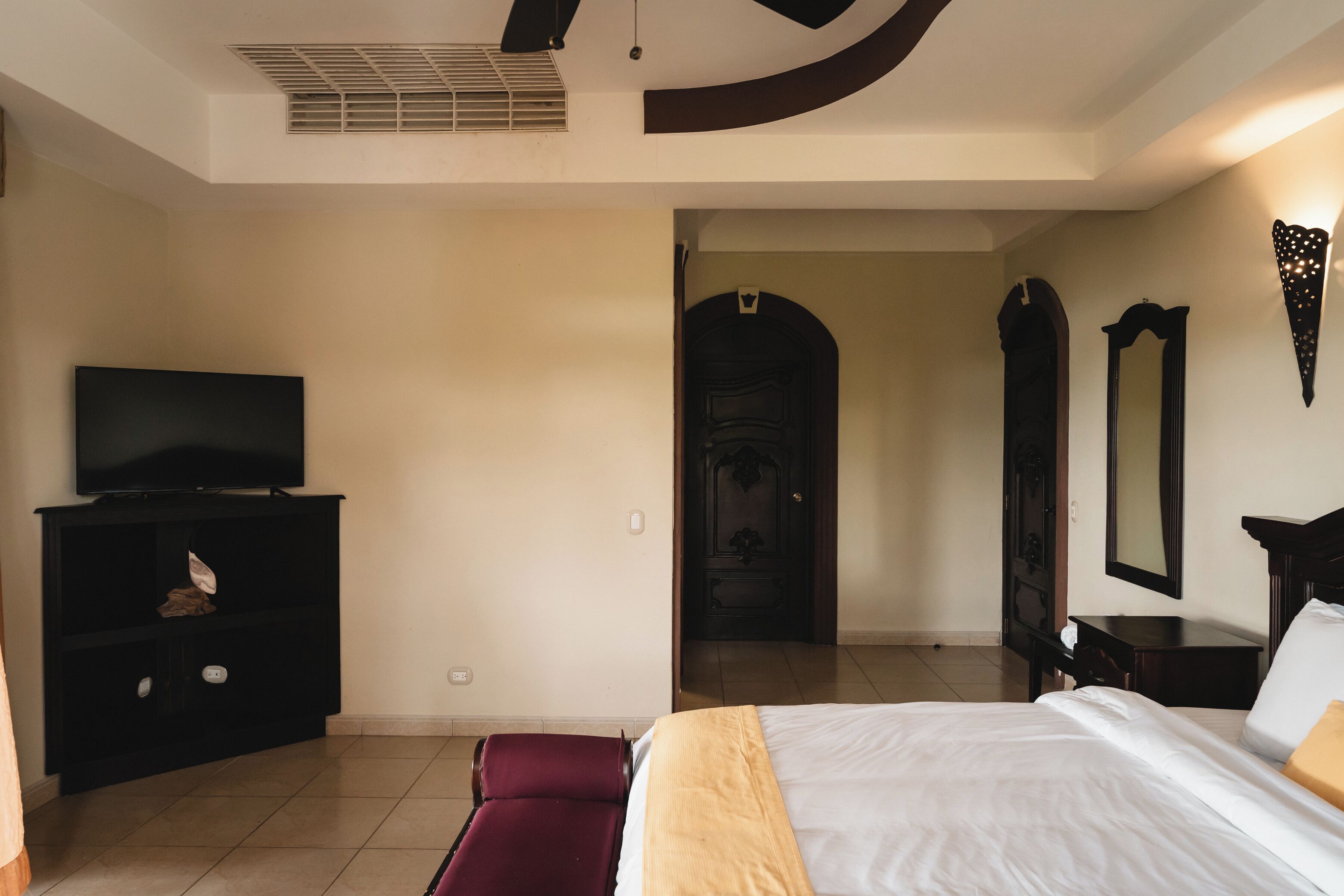 A hotel room with a bed, a TV on a stand, a wardrobe, and a door leading to another room.