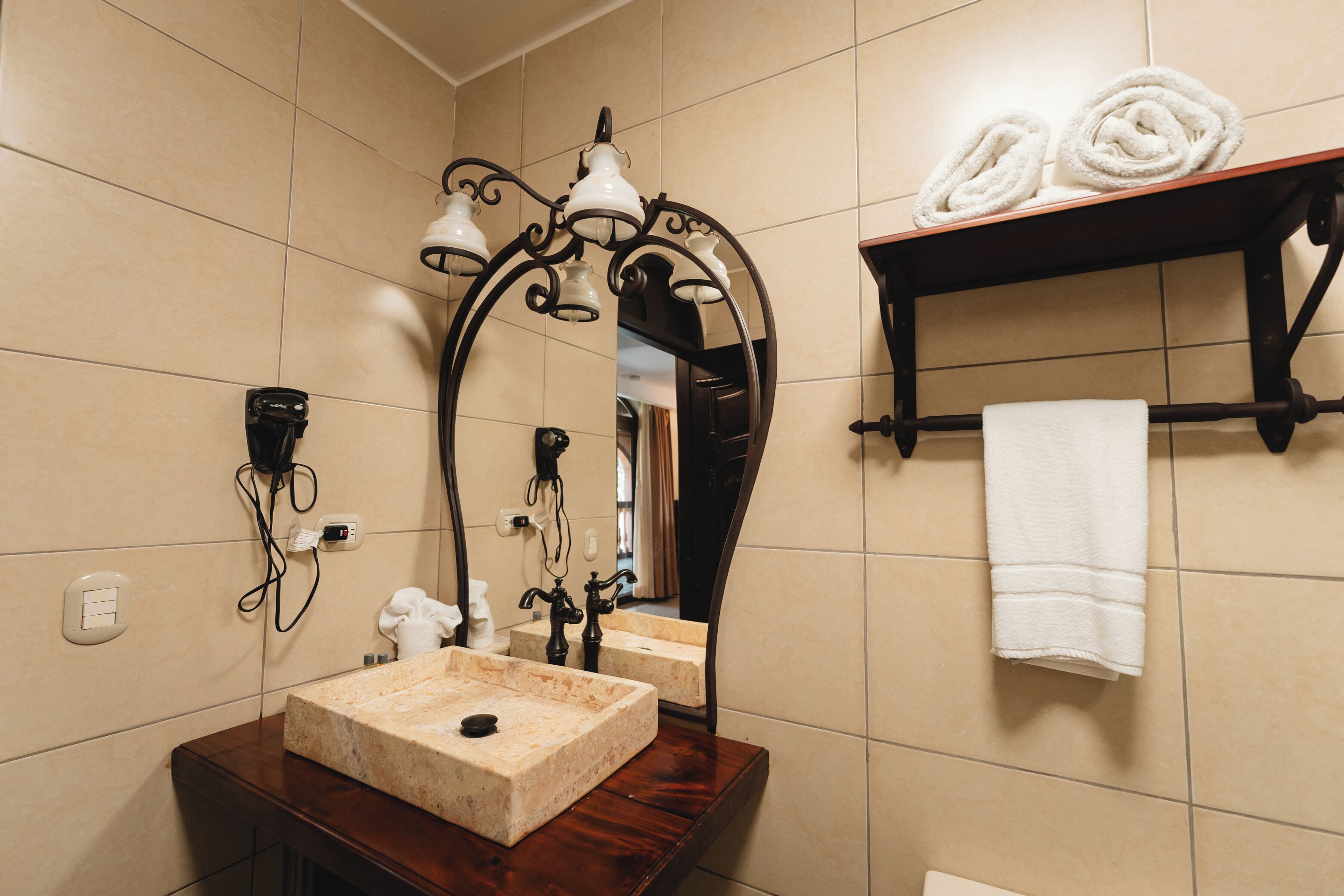 Un baño con lavamanos de mármol, un espejo con marco decorativo, un perchero con toallas y un calentador de pared.