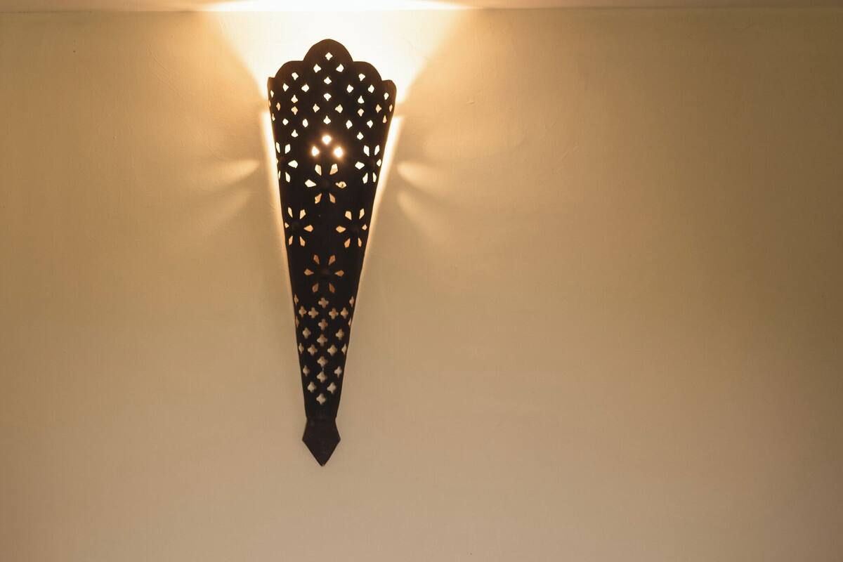 Un dormitorio con cabecera de madera, una mesita de noche con lámpara y una lámpara fijada a la pared.