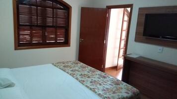 A bedroom with a bed, a wooden door, a television mounted on the wall, and a window with blinds.
