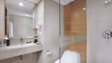 Un baño moderno con cabina de ducha de vidrio, un lavamanos blanco con espejo y una pared de acento de madera.