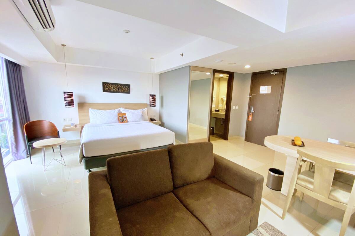 Ein modernes Hotelzimmer mit einem großen Bett, einer Couch, einem kleinen Tisch und einem durchgegangenen Tür erkennbaren Badezimmer.