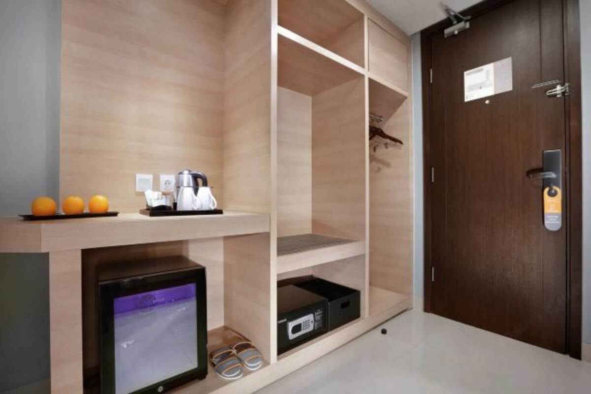 Une chambre d’hôtel avec un mur en bois, une télévision, une étagère avec des oranges, une machine à café et une porte avec une serrure.