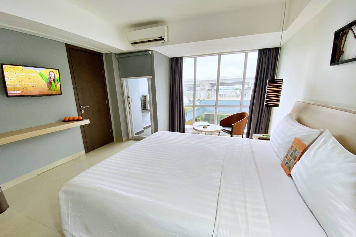 Ein Hotelzimmer mit einem großen Bett, einem an der Wand befestigten Fernseher, einem Balkon mit Aussicht und einem Sessel.