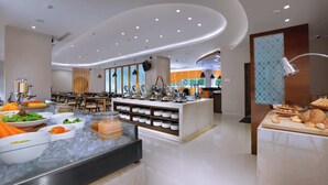 Een modern hotelrestaurant met een buffetopstelling, inclusief diverse gerechten en een zithoek met tafels en stoelen.