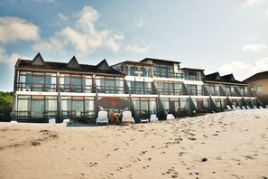 A beachfront hotel with multiple floors, large windows, and a sandy beach in front.