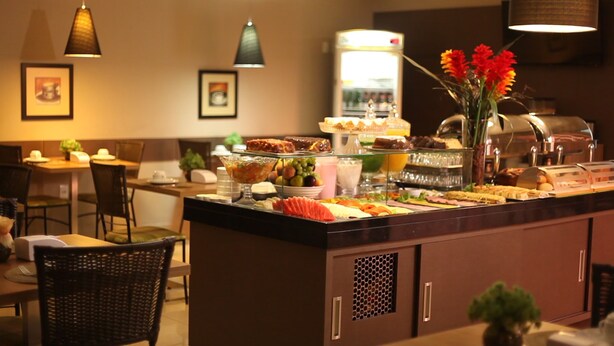 A buffet with various food items, a refrigerator, and a vase with flowers. - Hotel Horto (Rondonopolis)