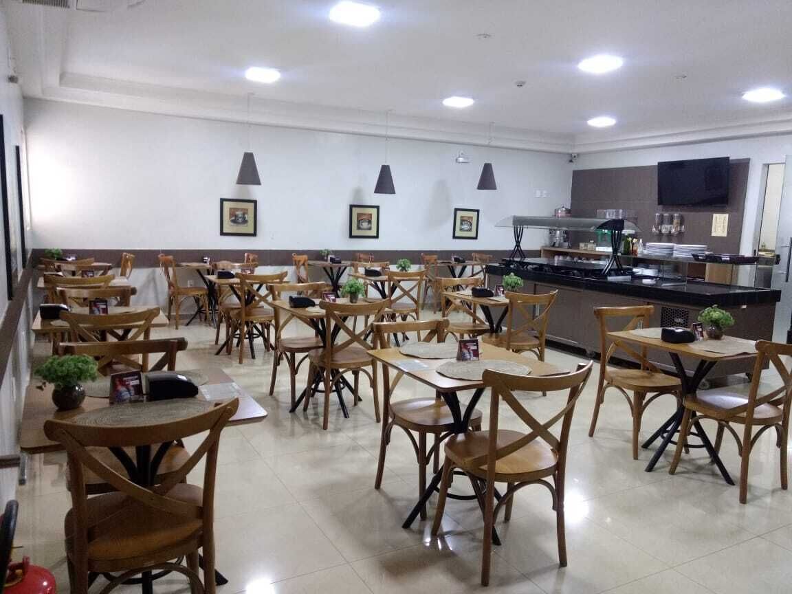 Un restaurante con mesas y sillas de madera, una zona de cocina y cuadros en la pared.