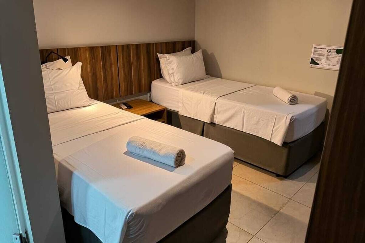Une chambre avec deux lits, une tête de lit en bois, une petite table et un panneau fixé au mur.