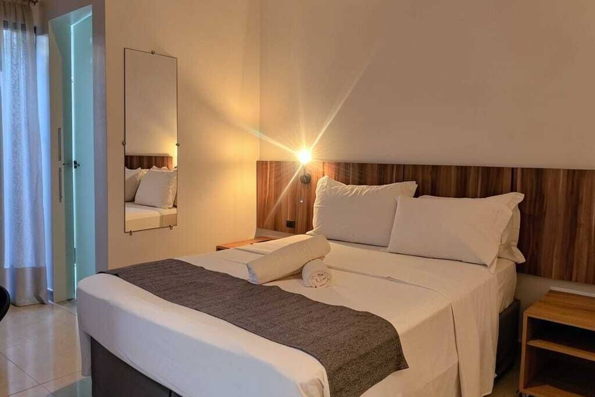 Une chambre d’hôtel avec un lit, des tables de chevet, un miroir et une porte.