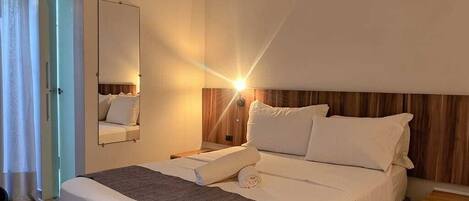 Una habitación de hotel con cama, mesitas de noche, un espejo y una puerta.