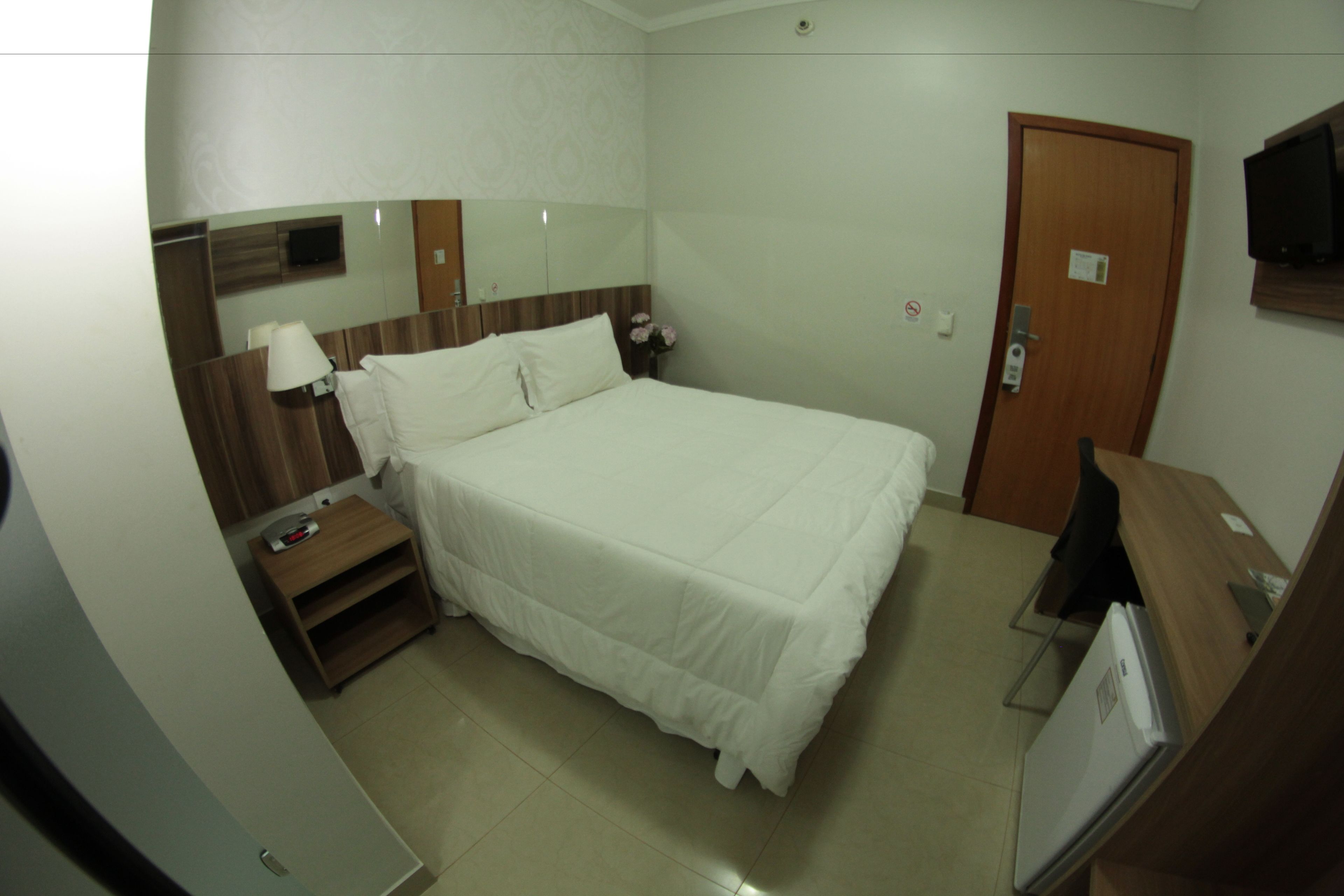 Una habitación de hotel con una cama, una mesita de noche, un televisor y una puerta.