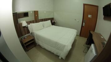 Una habitación de hotel con una cama, una mesita de noche, un televisor y una puerta.