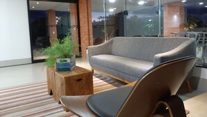A modern lobby with a grey sofa, a wooden coffee table, and a potted plant. - Hotel Horto (Rondonopolis)