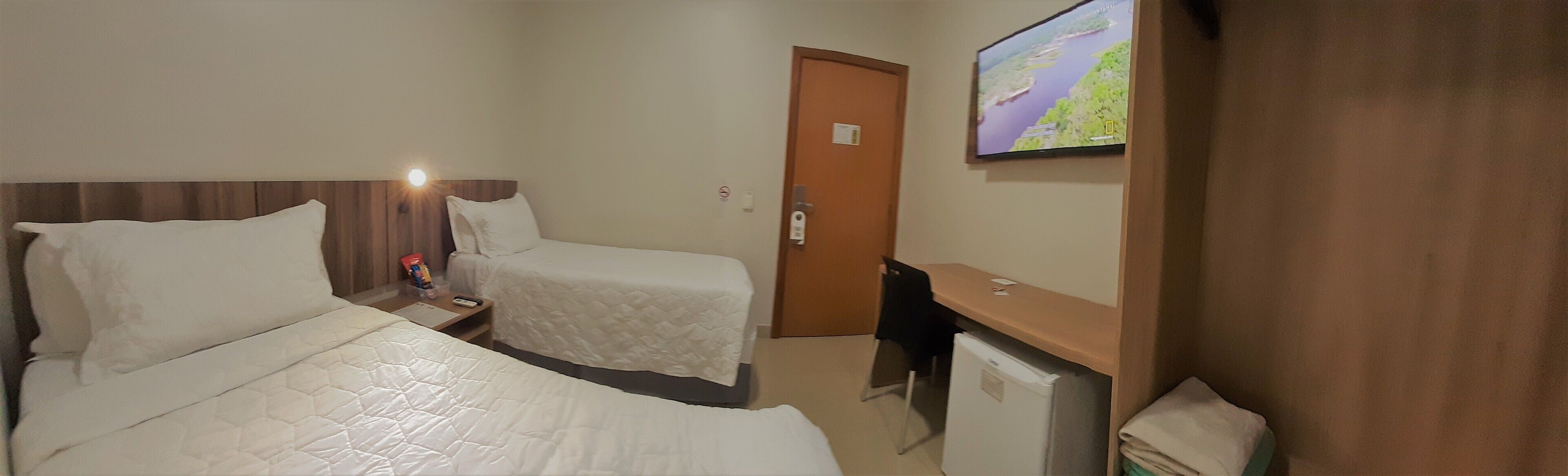 A hotel room with two beds, a desk, a TV, and a door.