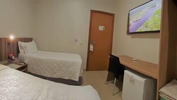 A hotel room with two beds, a desk, a TV, and a door.