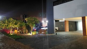 A nighttime outdoor area with a paved walkway, benches, and a building entrance. - Hotel Horto (Rondonopolis)