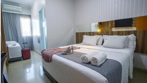 A hotel room with a bed, a TV, a suitcase, and a desk. - Hotel Horto (Rondonopolis)
