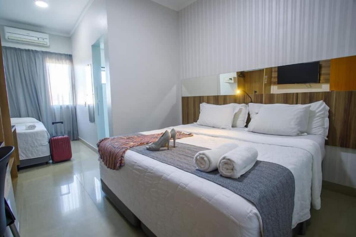 Une chambre d’hôtel avec un lit, une télévision, une valise et un bureau.