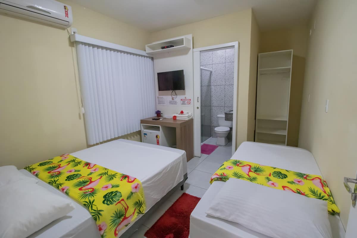 A hotel room with two beds, a desk, a TV, and a bathroom.