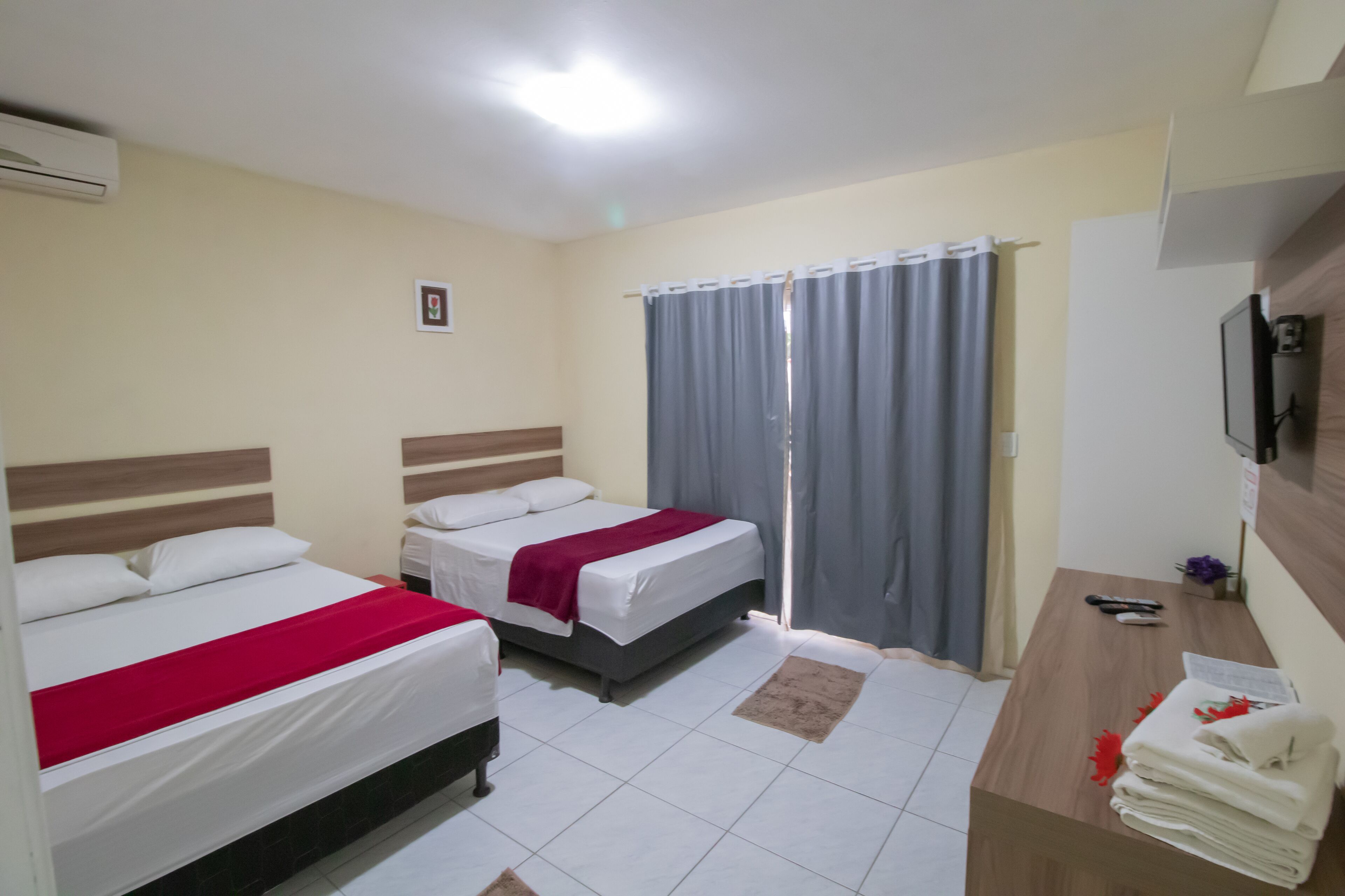 Habitació d'hotel amb dos llits, escriptori, televisió i finestra amb cortines.