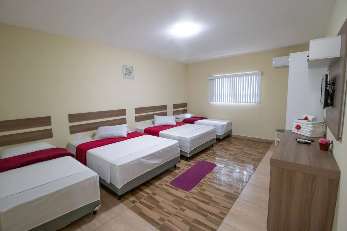 A hotel room with four single beds, a wooden desk, a mirror, and a window with blinds.