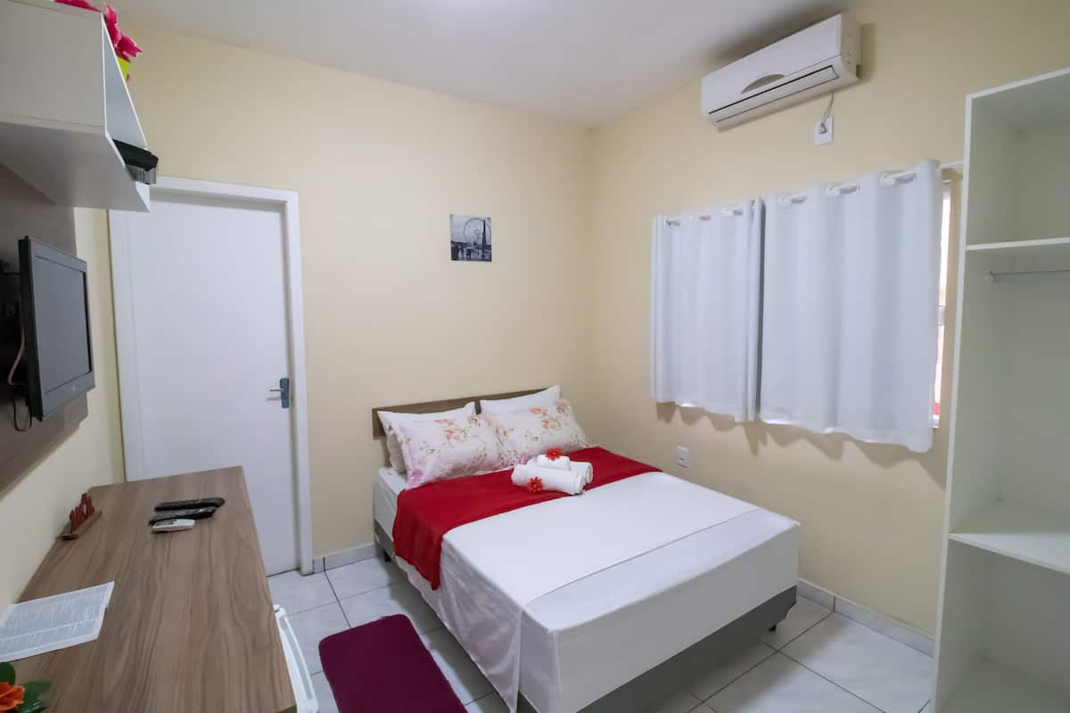 A bedroom with a bed, a desk, a chair, an air conditioner, and a window with curtains.