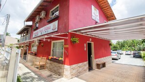 A red building with a covered patio area, a signboard, and a small garden with flowers.