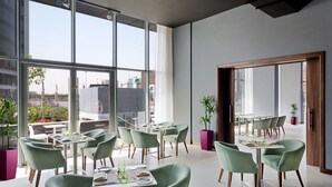 A modern dining area with green chairs and tables, large windows, and potted plants.