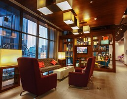 Un moderno vestíbulo de hotel con un sofá, dos sillones, un televisor y una zona de bar con taburetes.