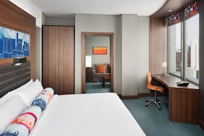 A hotel room with a large bed, a desk, a chair, and a window with a city view.