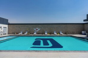A swimming pool with a large logo, sun loungers, and a wall with a decorative emblem.