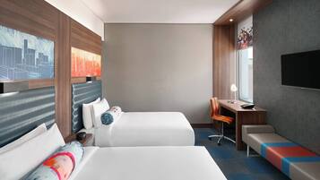 Habitación de hotel con dos camas, un escritorio, una silla, un banco, televisión y obras de arte en las paredes.