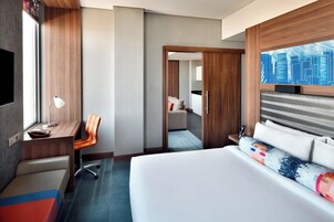 A hotel room with a bed, a desk, a chair, a TV, and a cityscape view.