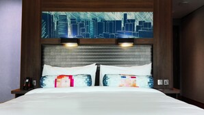 A hotel room with a large bed, two bedside lamps, and a cityscape artwork above the headboard.