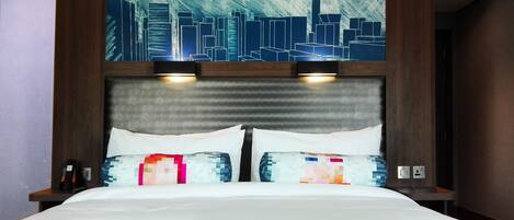 A hotel room with a large bed, two bedside lamps, and a cityscape artwork above the headboard.