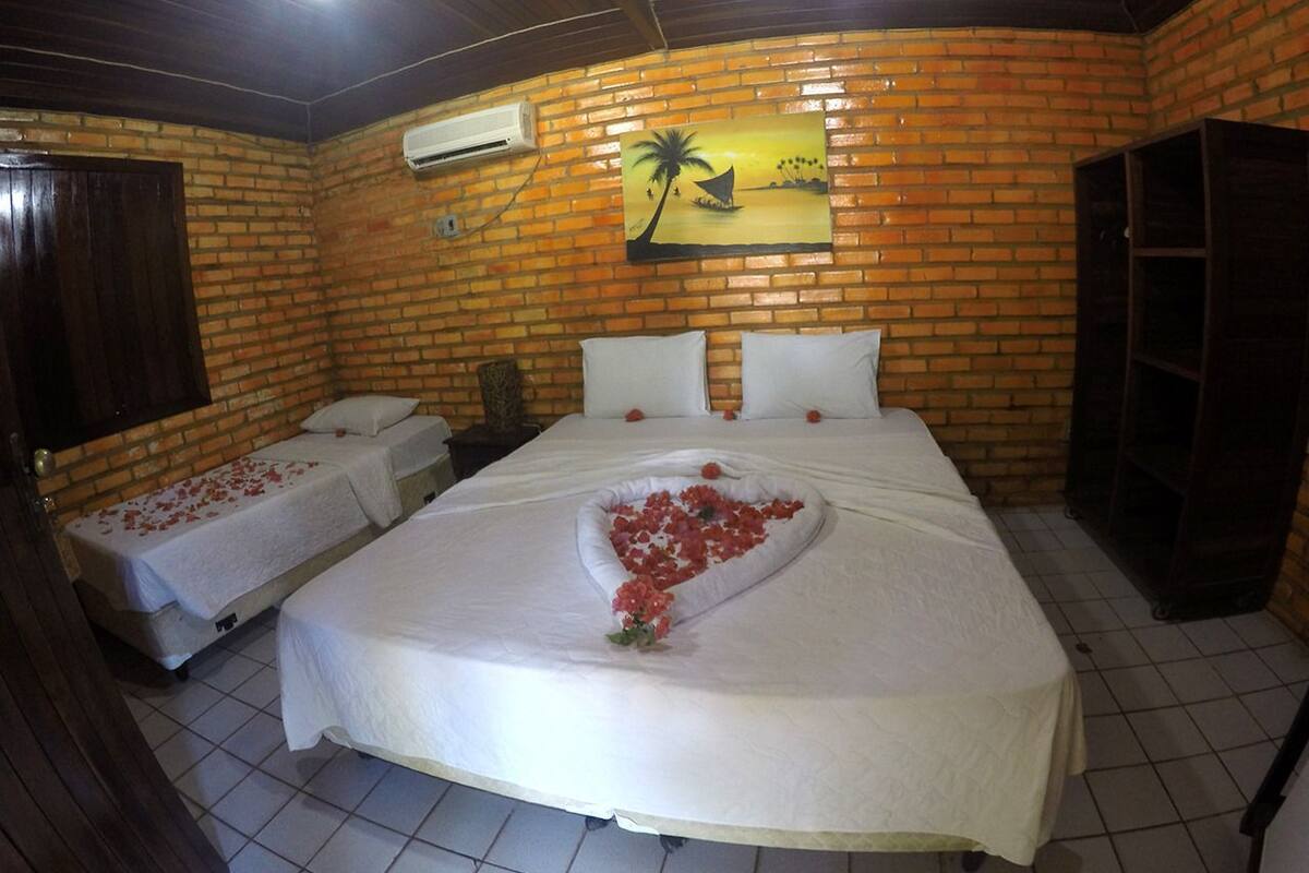 Una habitación con una cama grande, dos camas más pequeñas, una pared de ladrillo, un cuadro y un equipo de aire acondicionado.