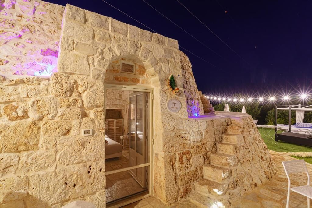 Un edificio de piedra con entrada de puerta de cristal, un pequeño balcón con planta decorativa y un cartel que indica un número de habitación.