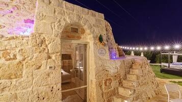 Un edificio de piedra con entrada de puerta de cristal, un pequeño balcón con planta decorativa y un cartel que indica un número de habitación.