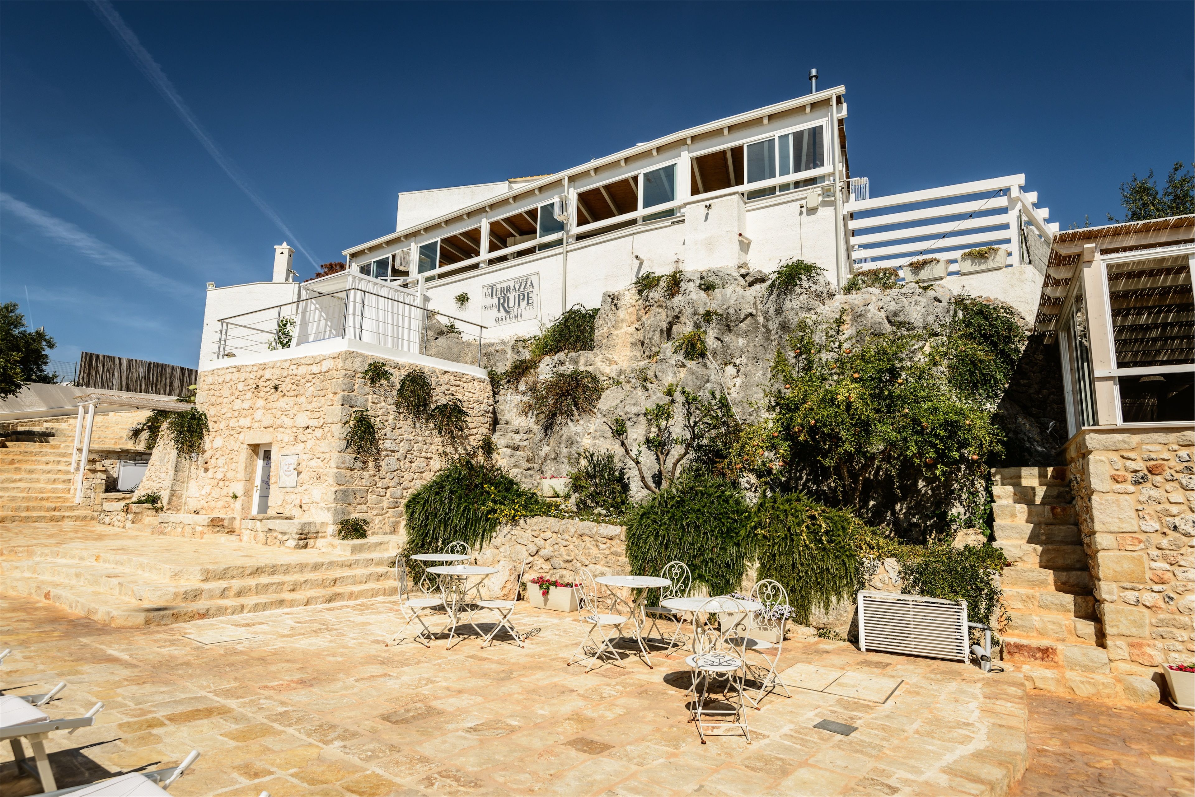 Un edificio moderno con fachada de piedra, zona de estar al aire libre y una escalera que conduce a los niveles superiores.