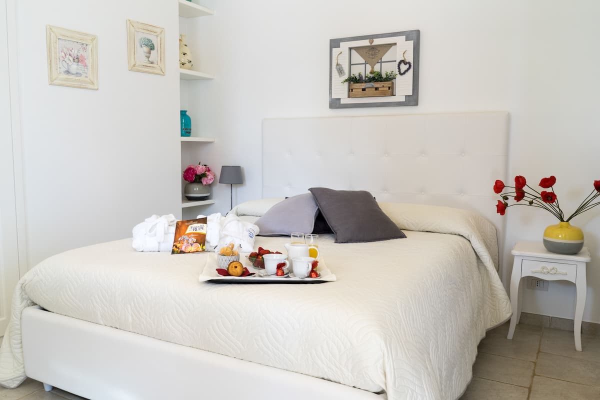 Ein ordentlich bezogenes Bett mit einem Tablett Frühstücksgebäck, ein Nachttisch mit Blumen in einer Vase und eine Wand mit gerahmten Bildern.