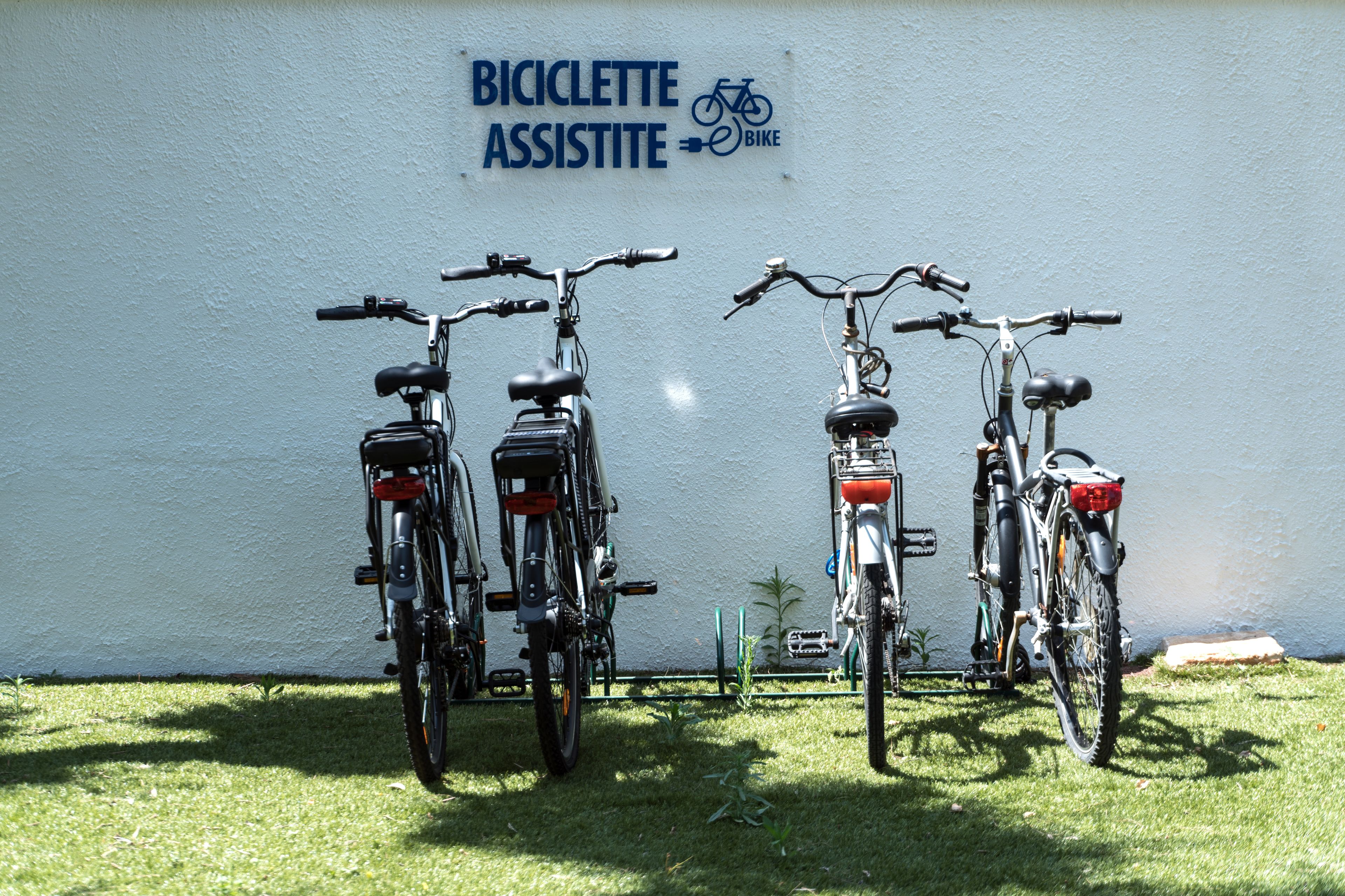 Three bicycles parked against a wall with a sign that reads "BICICLETTE ASSISTITE BIKE".