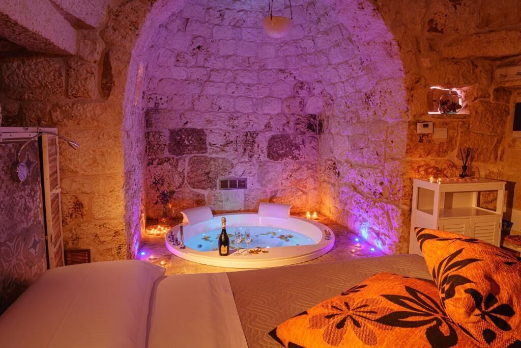 A stone-walled room with a circular hot tub, a bed with white bedding, and a decorative pillow.