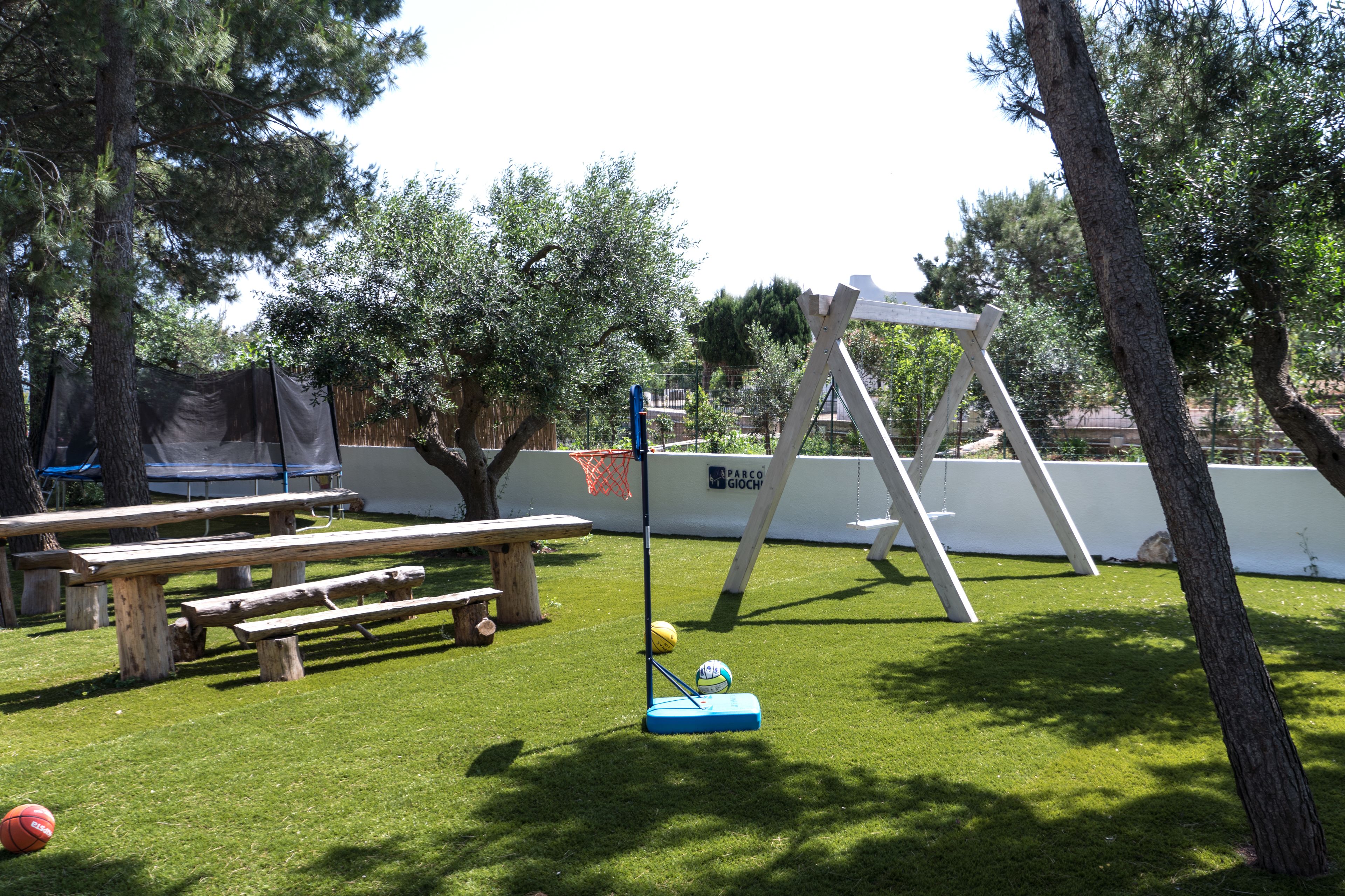 A grassy outdoor area with picnic tables, a swing set, and a basketball hoop.