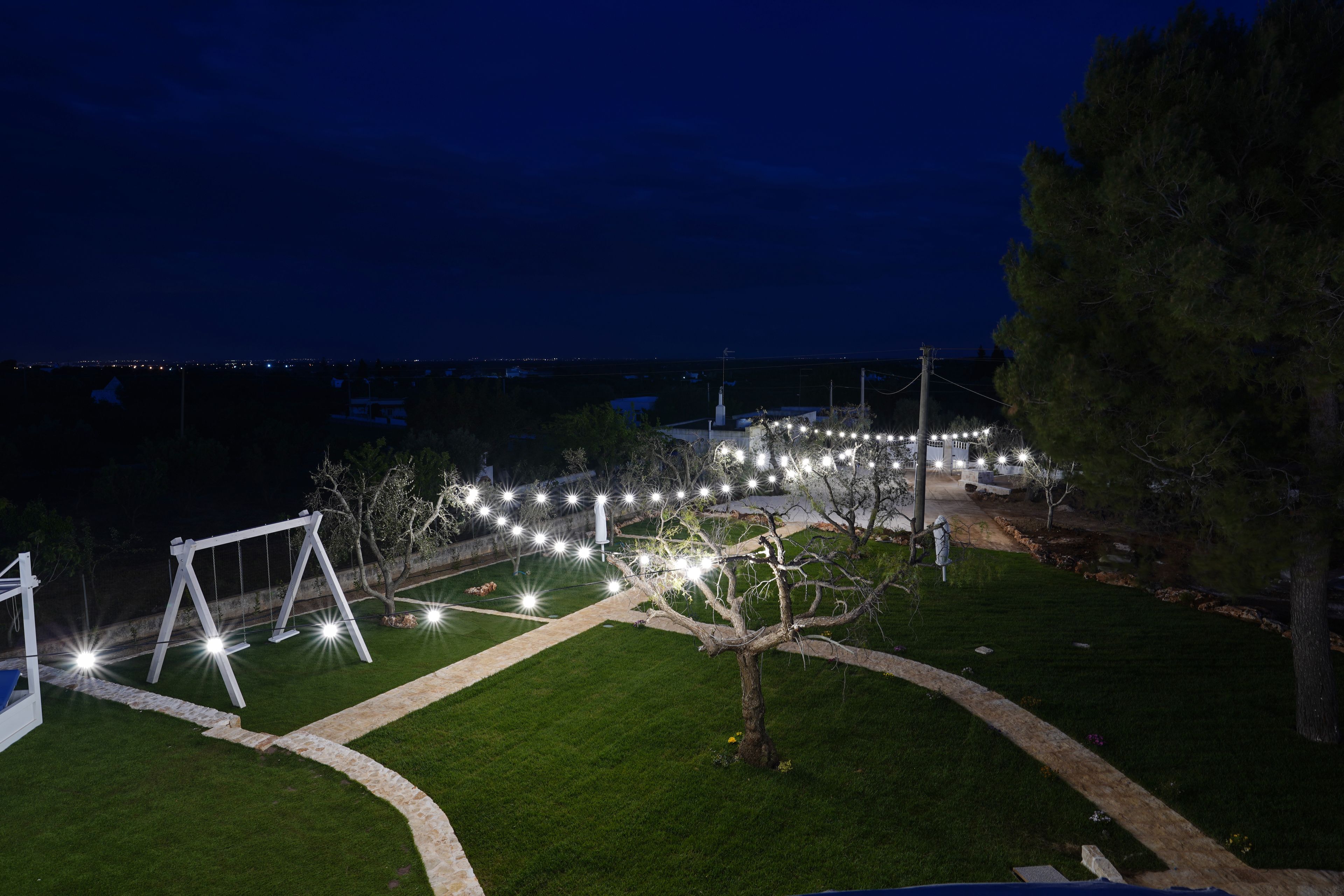 A nighttime view of a well-lit outdoor area with a swing set, a tree, and a pathway.