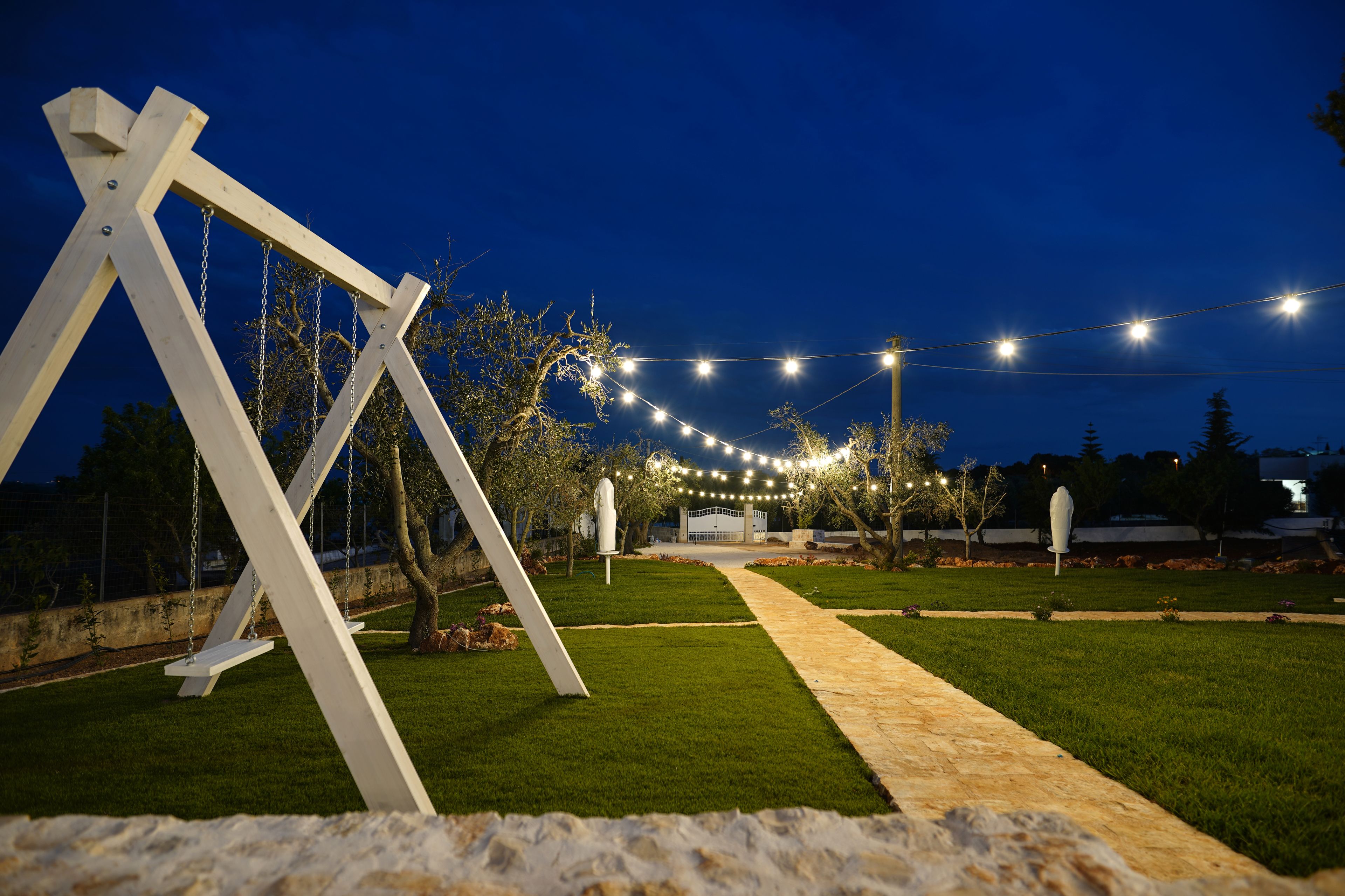 Un espace extérieur aménagé pour les soirées, avec une balançoire, un sentier et des guirlandes lumineuses.