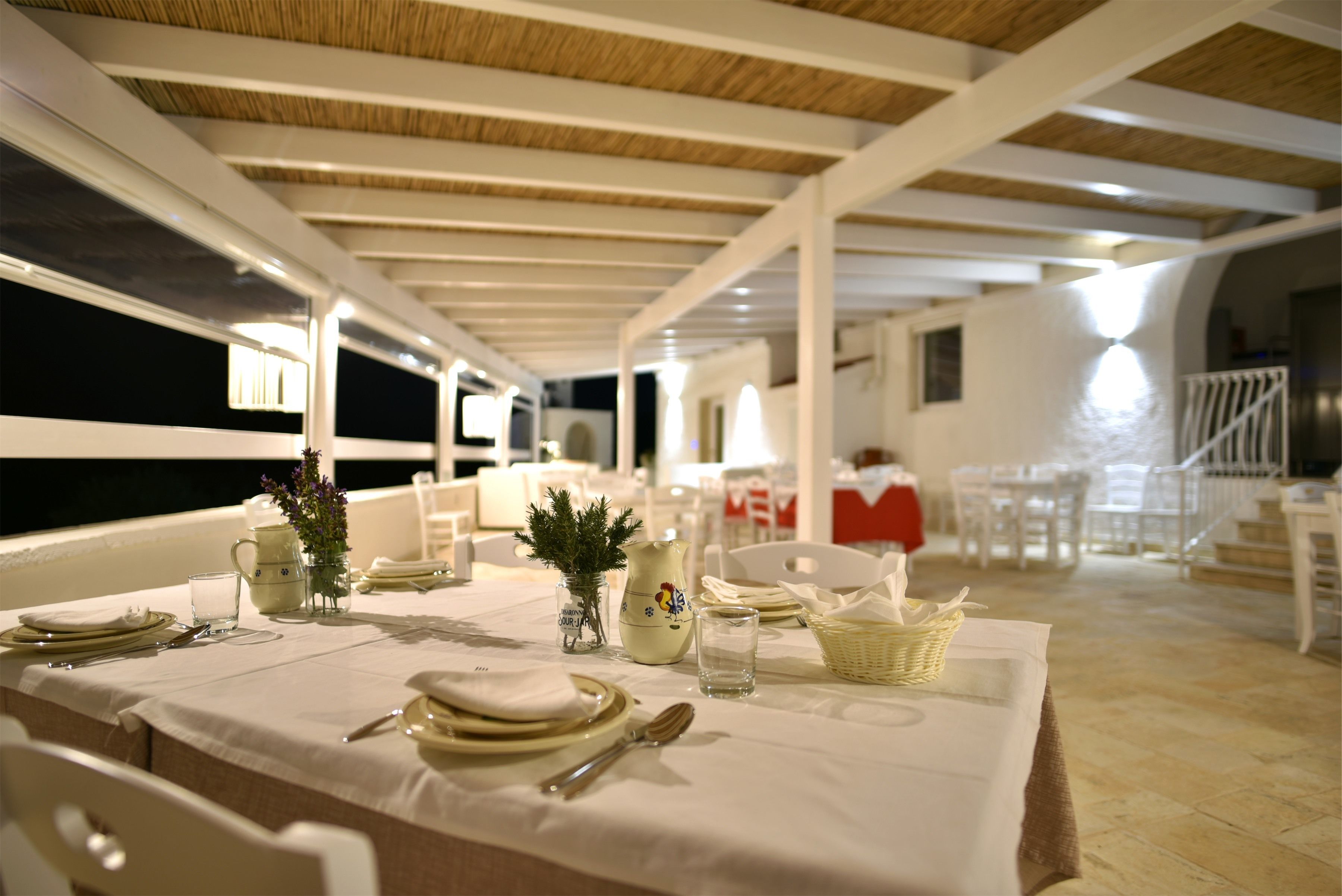 Un espace repas avec une longue table dressée pour le repas, des chaises blanches et un plafond orné de poutres en bois.