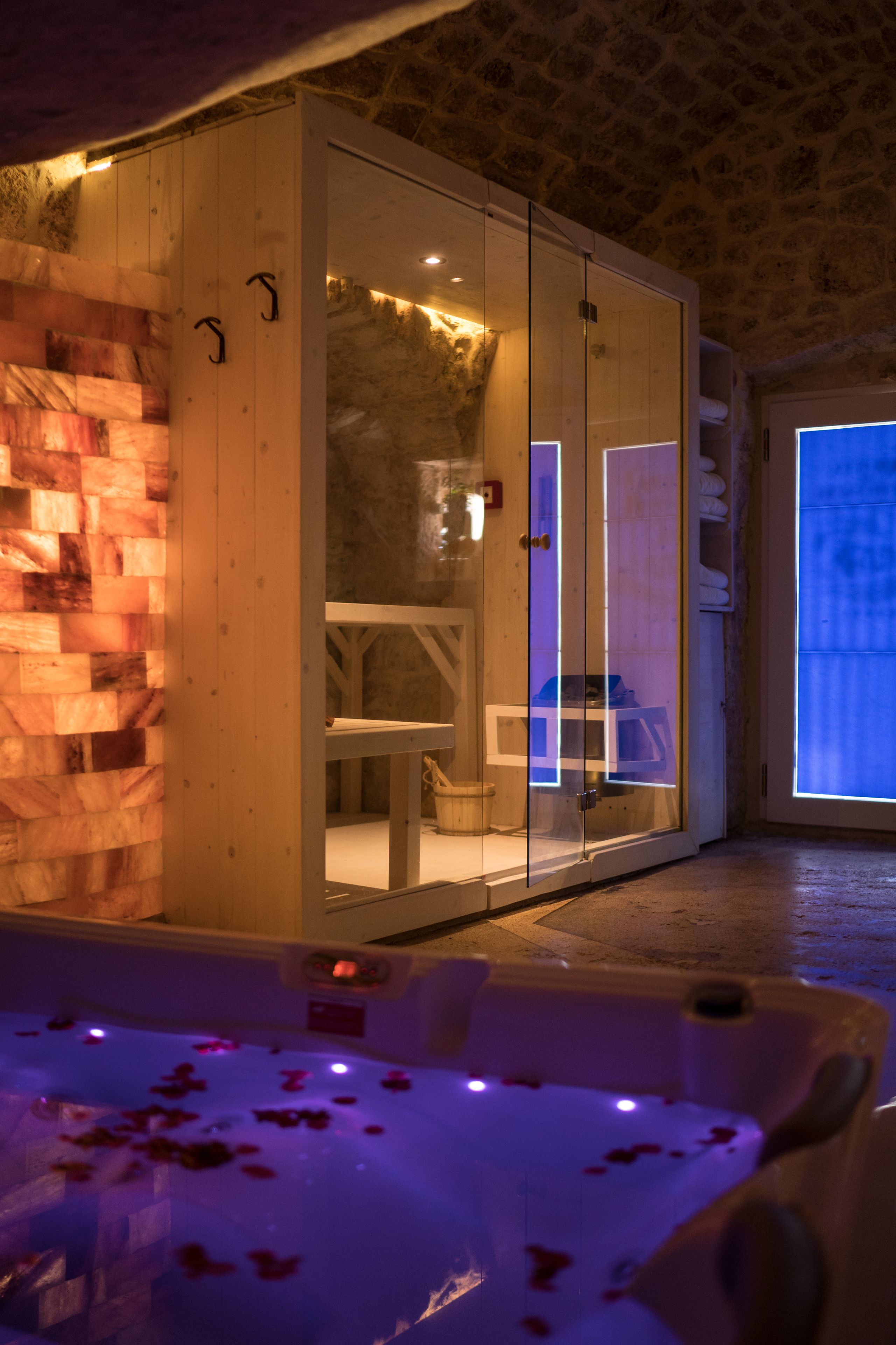 Ein Spa-Raum mit Glastrennwand, einer Holzwand und einer Badewanne mit Rosenblüten.