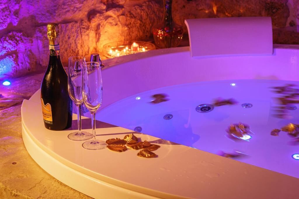 Una vasca idromassaggio con champagne e bicchieri su una superficie in pietra.